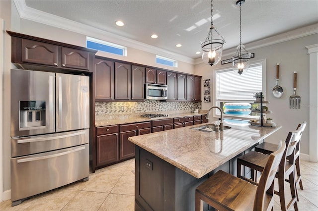 kitchen with pendant lighting, appliances with stainless steel finishes, a sink, dark brown cabinets, and light stone countertops