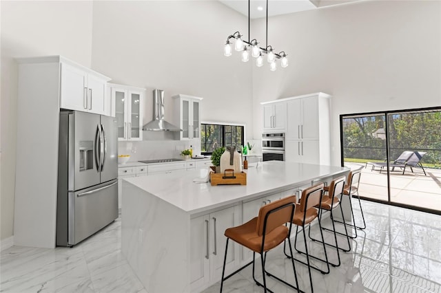 kitchen with white cabinets, wall chimney exhaust hood, a large island, marble finish floor, and stainless steel appliances