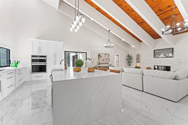 kitchen with marble finish floor, a notable chandelier, double oven, white cabinetry, and beam ceiling