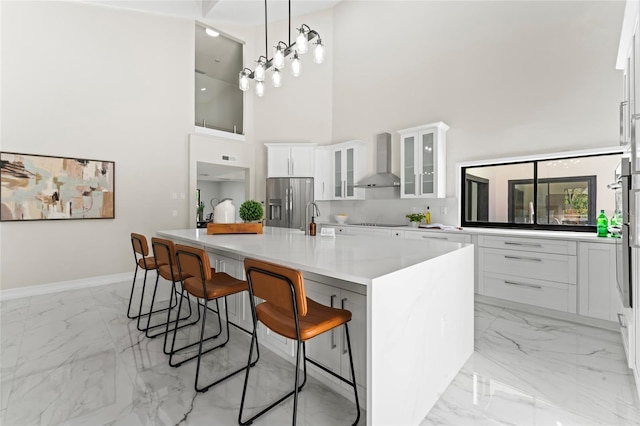 kitchen featuring marble finish floor, a breakfast bar area, white cabinetry, wall chimney range hood, and stainless steel fridge with ice dispenser