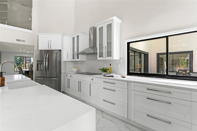 kitchen featuring marble finish floor, white cabinetry, wall chimney range hood, stainless steel fridge, and black electric cooktop