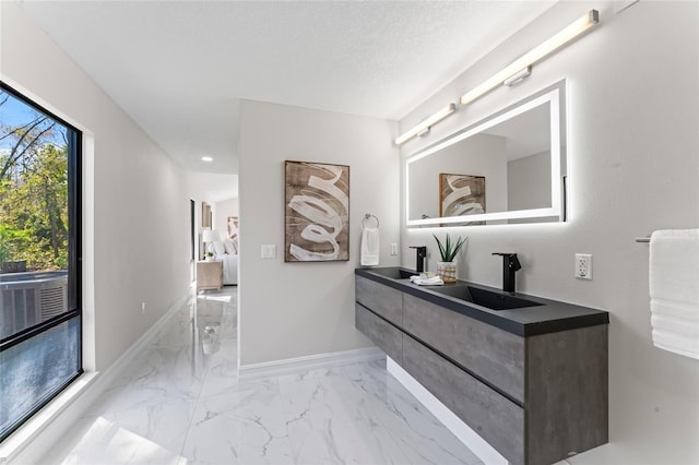 interior space with a textured ceiling, a sink, baseboards, marble finish floor, and double vanity