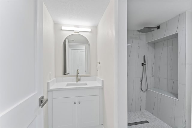 full bath with a textured ceiling, a marble finish shower, and vanity