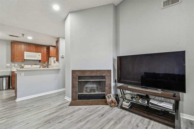 living room with light wood-style flooring, a fireplace, and visible vents