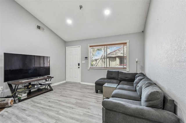 living room featuring lofted ceiling, visible vents, baseboards, and wood finished floors