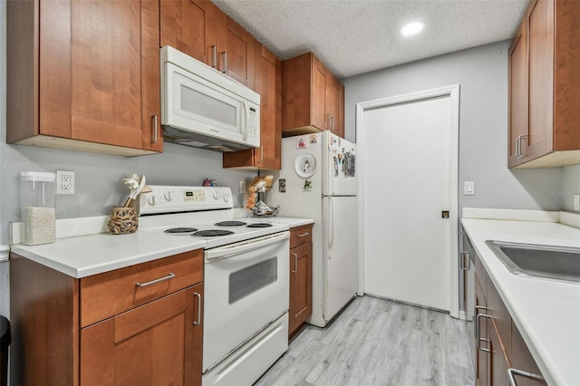 kitchen with a textured ceiling, white appliances, light countertops, brown cabinets, and light wood finished floors