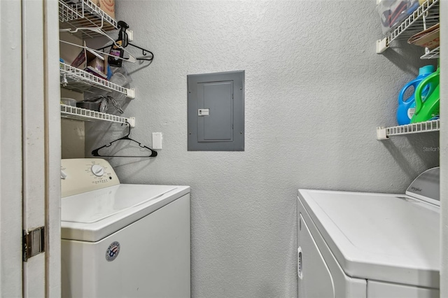 washroom with electric panel, a textured wall, and washer and clothes dryer