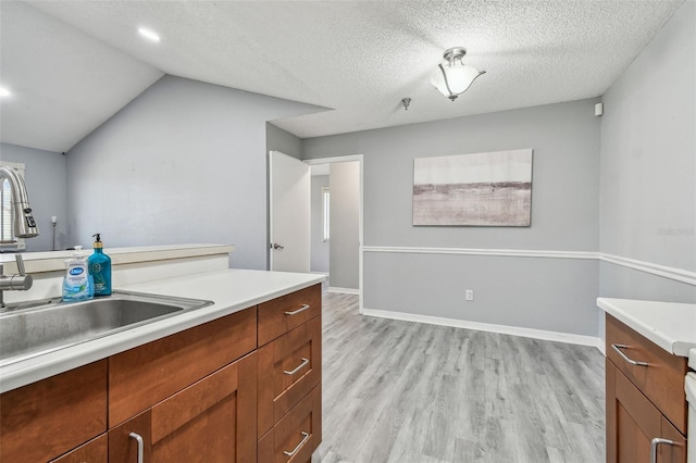 kitchen with light wood-style floors, vaulted ceiling, light countertops, and a sink