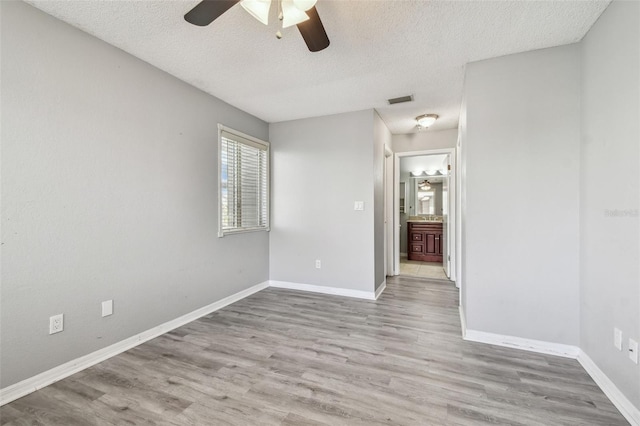 empty room with visible vents, a textured ceiling, baseboards, and wood finished floors