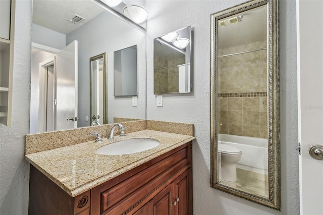 full bathroom with toilet, vanity, visible vents, and a textured wall