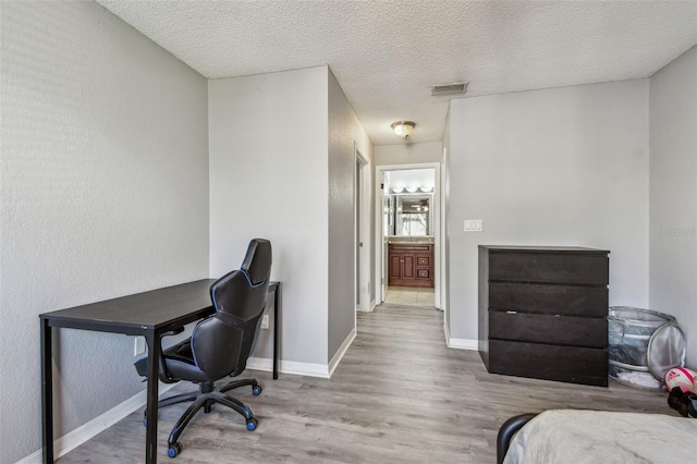 office with a textured ceiling, wood finished floors, visible vents, and baseboards