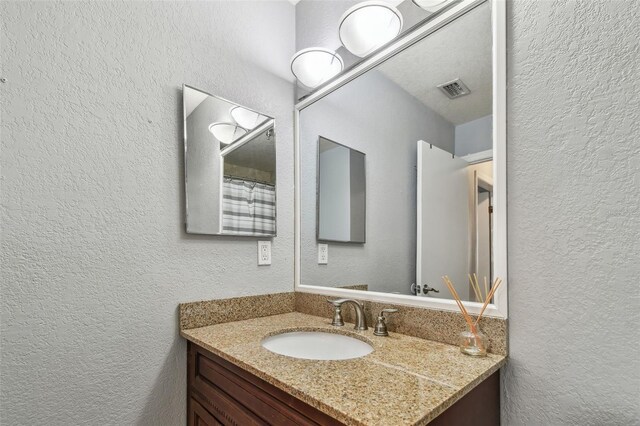 bathroom featuring visible vents, a textured wall, and vanity