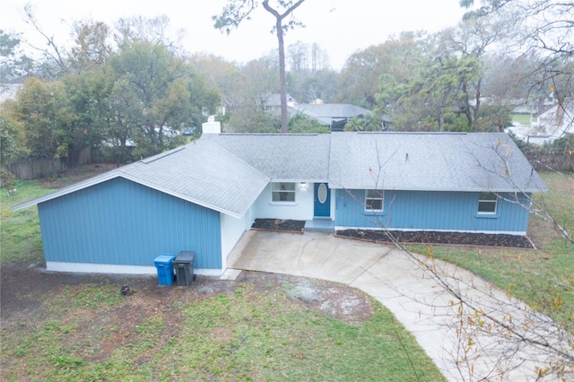 view of front facade featuring driveway, a shingled roof, a chimney, and a front lawn