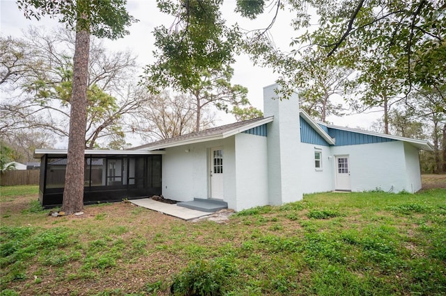 rear view of property featuring a sunroom, a yard, a chimney, and a patio