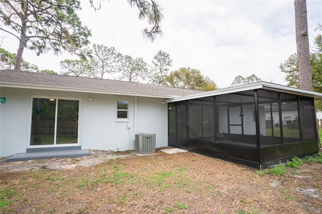 rear view of property featuring central AC unit, roof with shingles, a sunroom, and stucco siding