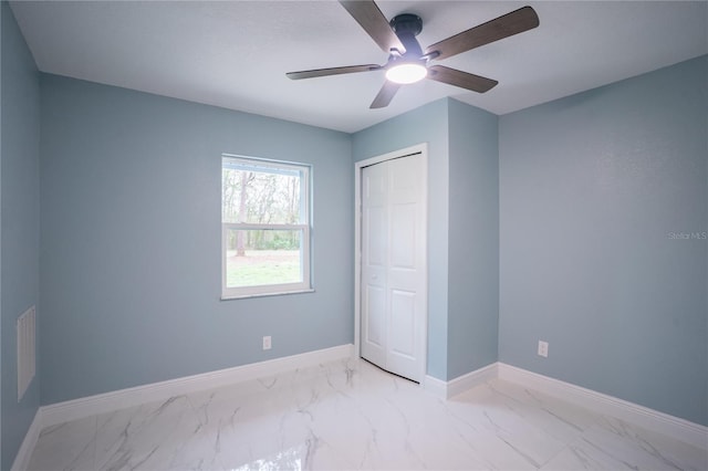 unfurnished bedroom with marble finish floor, a ceiling fan, baseboards, and a closet
