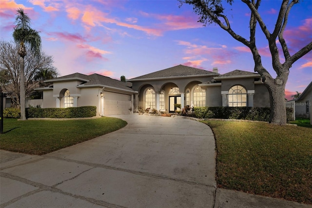 mediterranean / spanish-style home with a garage, driveway, a front lawn, and stucco siding