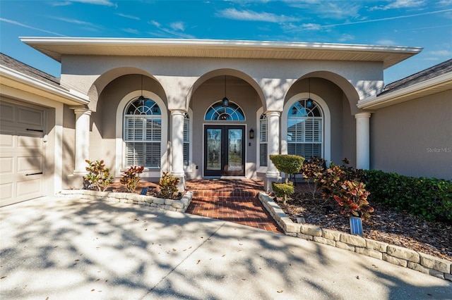 entrance to property featuring french doors, covered porch, an attached garage, and stucco siding