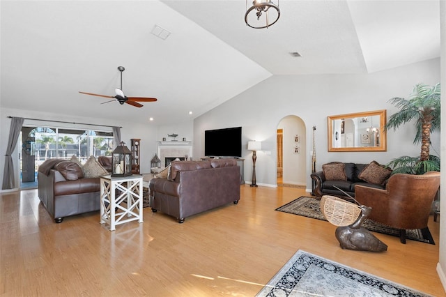 living room with arched walkways, ceiling fan, a fireplace, light wood-style floors, and vaulted ceiling