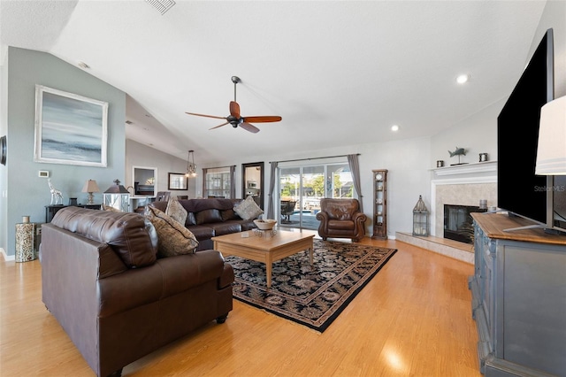 living area featuring lofted ceiling, a fireplace, visible vents, a ceiling fan, and light wood finished floors