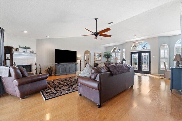 living room with arched walkways, french doors, a fireplace, lofted ceiling, and light wood-style floors