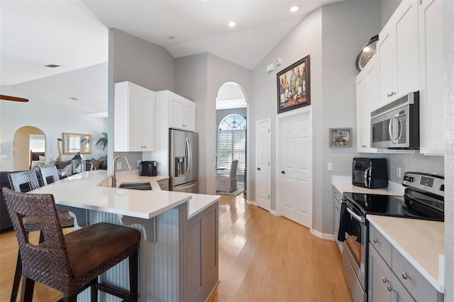 kitchen featuring arched walkways, a breakfast bar, vaulted ceiling, stainless steel appliances, and a sink