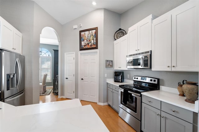 kitchen featuring stainless steel appliances, arched walkways, light countertops, and gray cabinetry