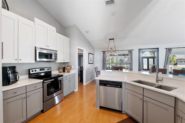 kitchen featuring stainless steel appliances, a sink, visible vents, vaulted ceiling, and gray cabinets