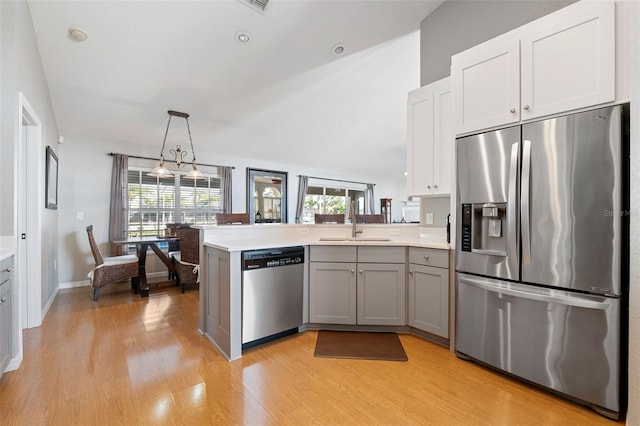 kitchen with light wood finished floors, light countertops, appliances with stainless steel finishes, a sink, and a peninsula