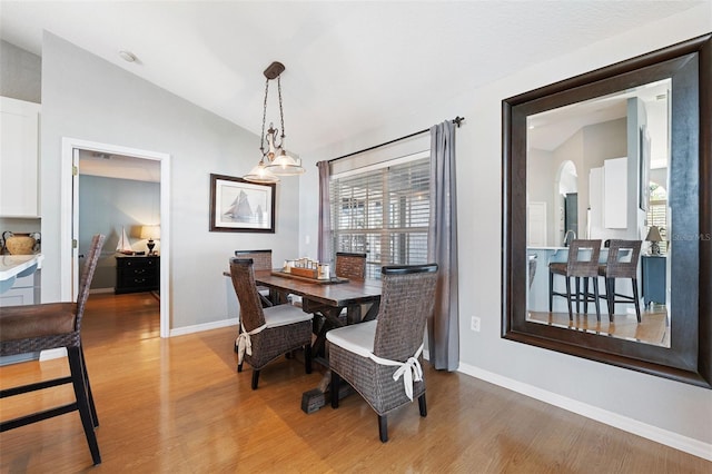 dining space with arched walkways, baseboards, vaulted ceiling, and light wood finished floors