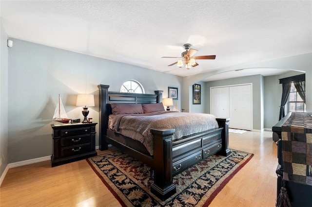 bedroom with light wood-style floors, baseboards, arched walkways, and a closet