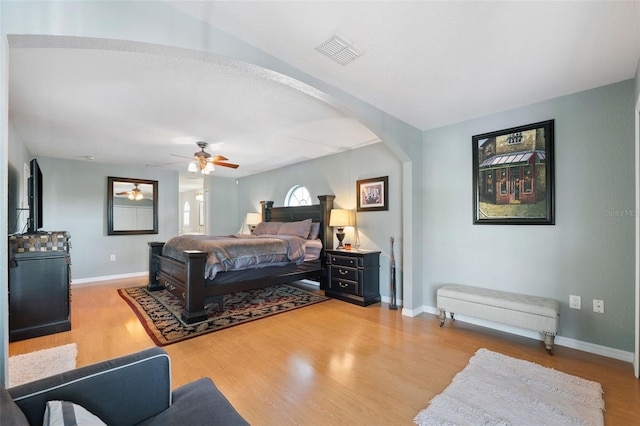 bedroom with arched walkways, visible vents, ceiling fan, wood finished floors, and baseboards