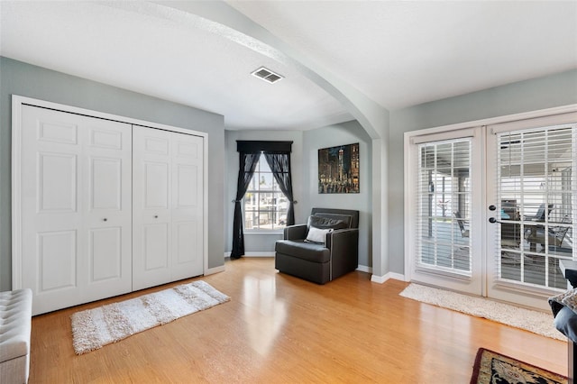 sitting room with arched walkways, visible vents, baseboards, light wood-style floors, and french doors