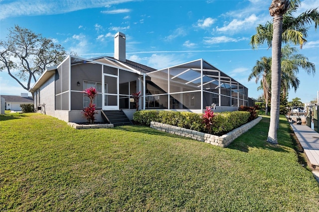 back of house with glass enclosure, a lawn, a chimney, and stucco siding