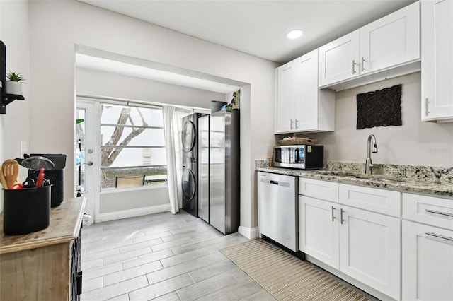 kitchen with white cabinets, light stone counters, stacked washer / drying machine, stainless steel appliances, and a sink