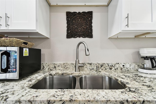 kitchen featuring light stone countertops, stainless steel microwave, a sink, and white cabinetry