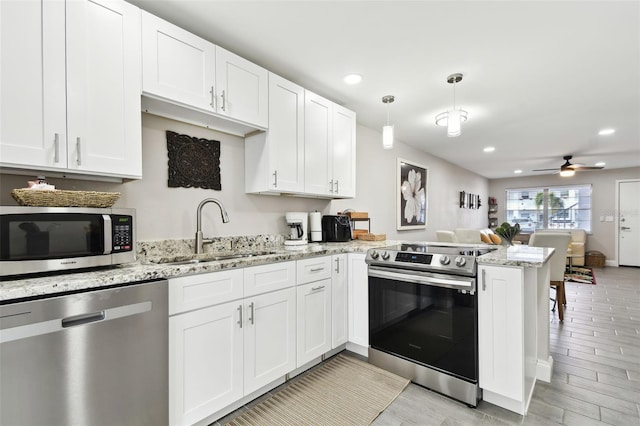 kitchen with white cabinets, open floor plan, a peninsula, stainless steel appliances, and a sink