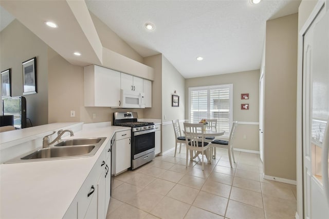 kitchen with a sink, light countertops, light tile patterned floors, gas range, and white microwave