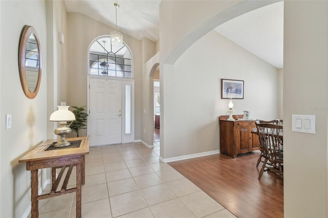 entryway with baseboards, high vaulted ceiling, an inviting chandelier, arched walkways, and light wood-type flooring