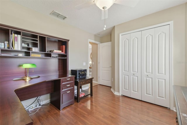 office area with visible vents, a textured ceiling, wood finished floors, baseboards, and ceiling fan