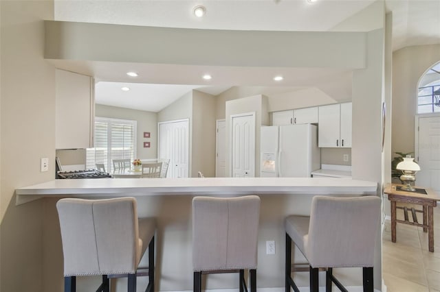 kitchen featuring a breakfast bar, light countertops, white refrigerator with ice dispenser, and white cabinetry