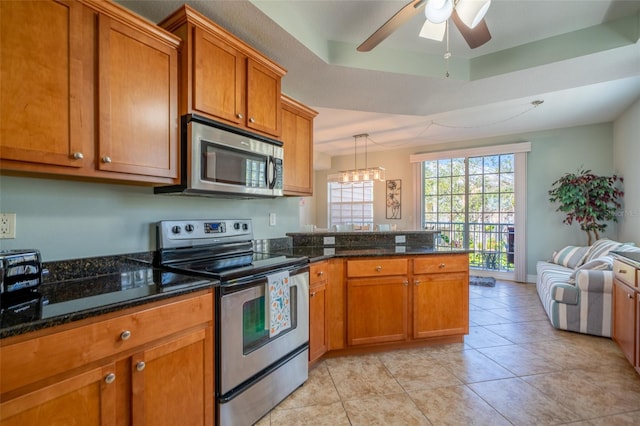 kitchen featuring a tray ceiling, light tile patterned floors, appliances with stainless steel finishes, brown cabinetry, and a peninsula