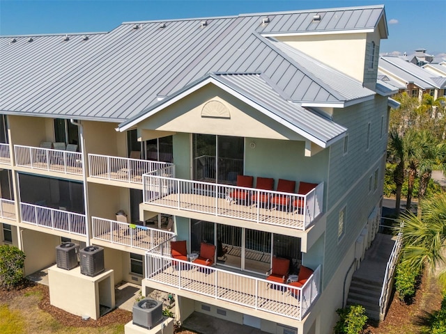 rear view of property with metal roof, central AC, stairway, stucco siding, and a standing seam roof