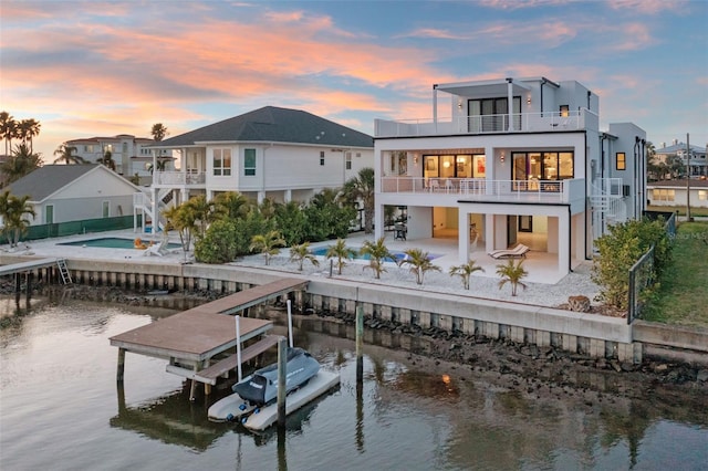 back of property at dusk featuring a patio, a water view, boat lift, and a balcony