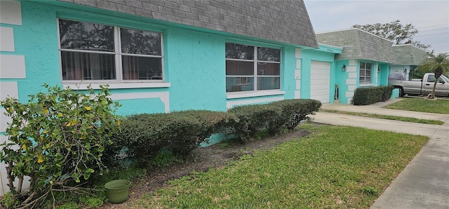 view of side of property featuring a garage, stucco siding, roof with shingles, and mansard roof