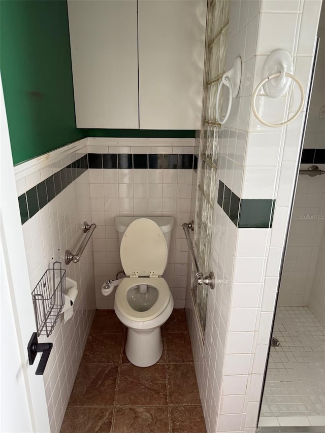 full bath featuring toilet, a stall shower, tile patterned flooring, and tile walls