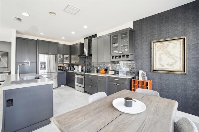 kitchen featuring stainless steel appliances, visible vents, gray cabinetry, a sink, and wall chimney exhaust hood