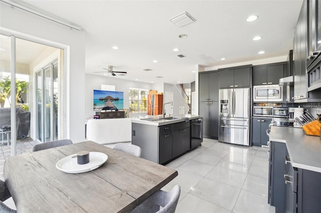 kitchen with light tile patterned flooring, stainless steel appliances, visible vents, backsplash, and an island with sink