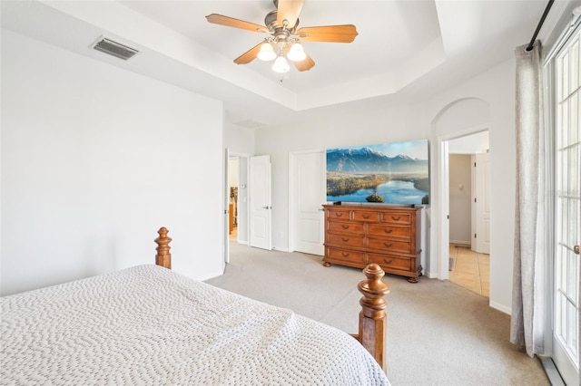 bedroom with light colored carpet, a tray ceiling, visible vents, and a ceiling fan