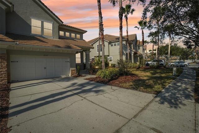 exterior space with a garage, concrete driveway, a tile roof, and stucco siding